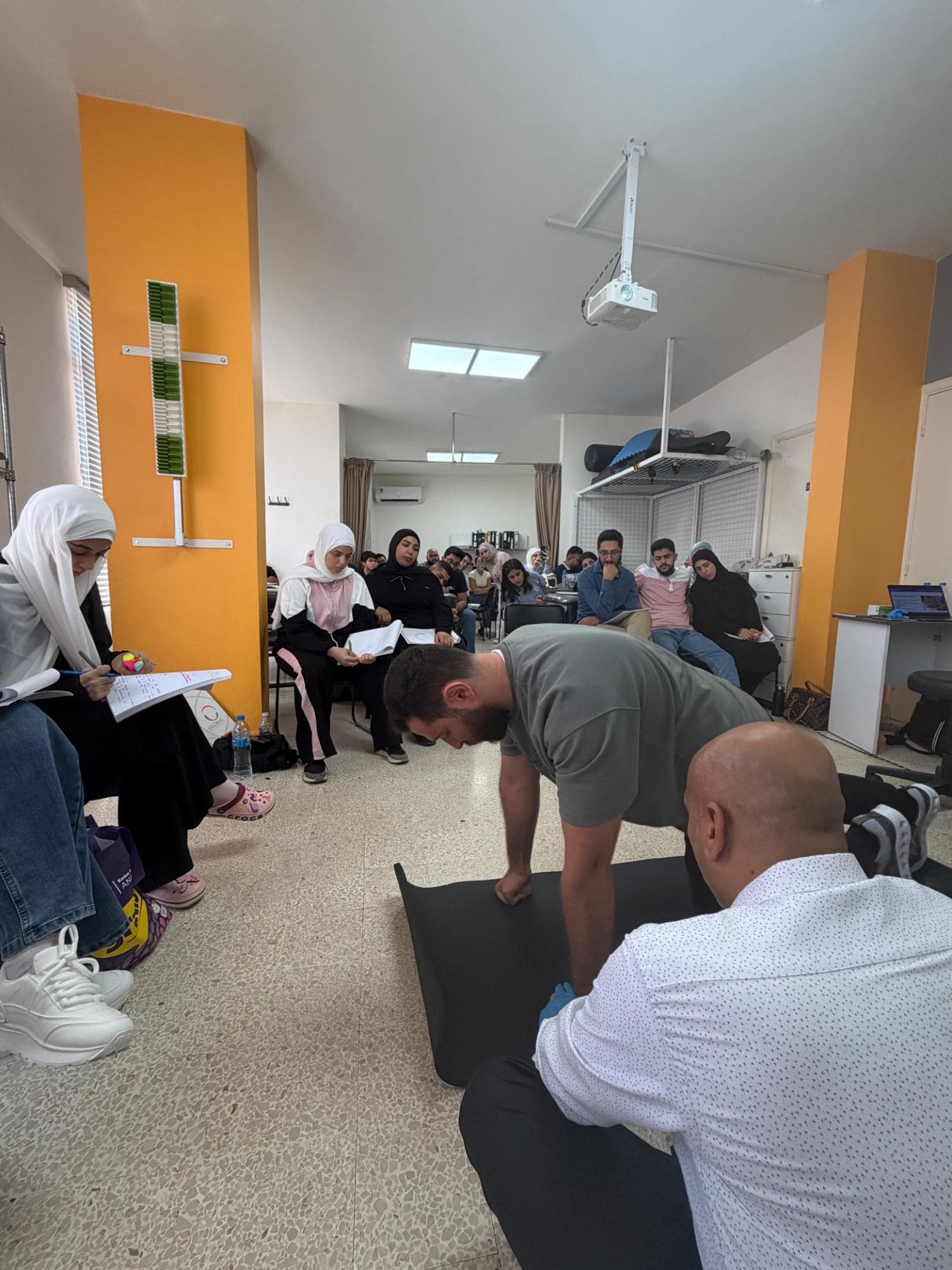 Dr. Hussein Nasser demonstrates an ankle and foot manual therapy technique on a participant while seated students take notes during the Mulligan workshop