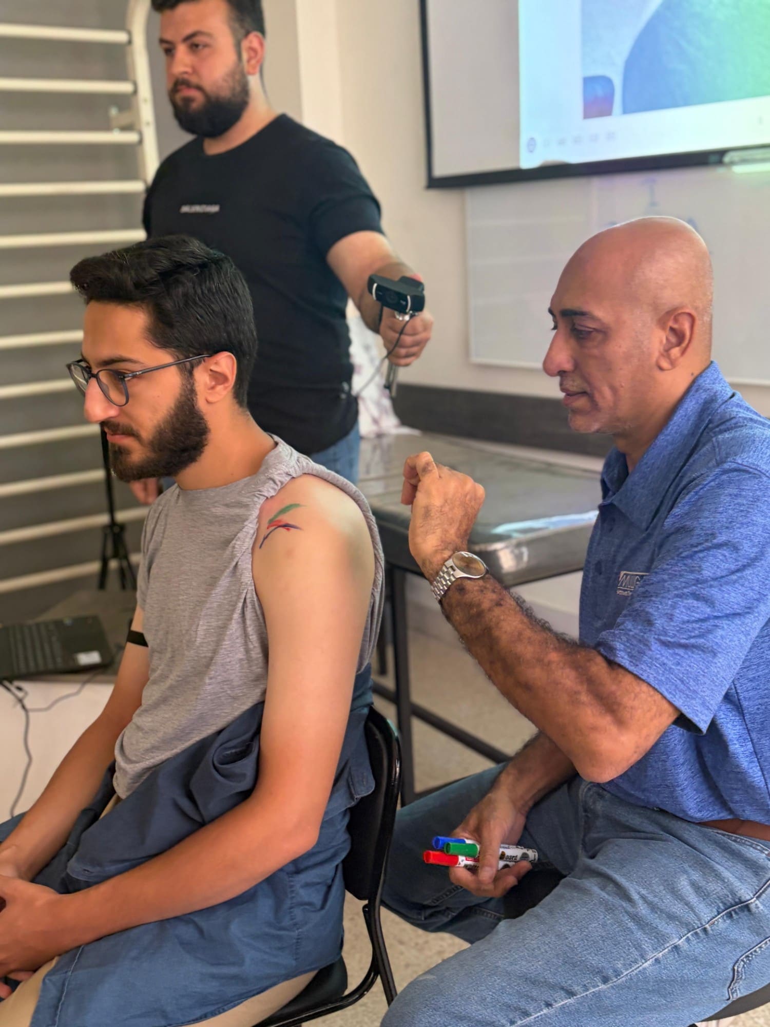 Dr. Hussein Nasser explains a technique to a seated participant with an X-ray image displayed on a nearby laptop