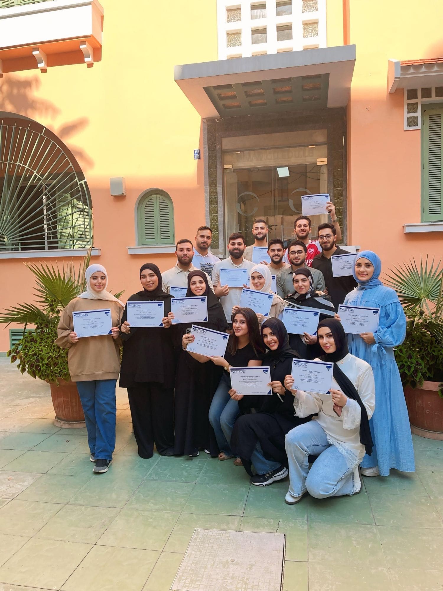 Workshop attendees hold their certificates of attendance in front of the building entrance