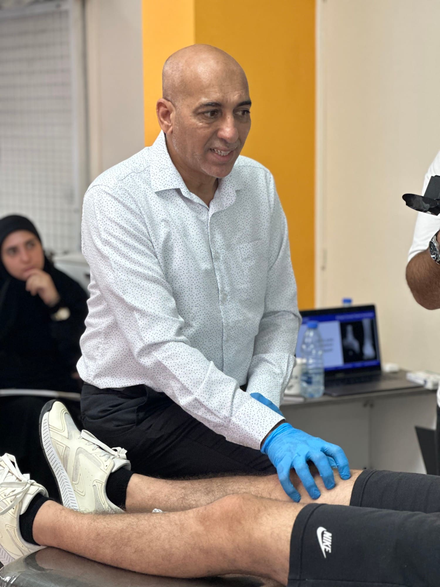 Dr. Hussein Nasser assesses a participant's knee on the treatment table with an X-ray image shown on a laptop screen